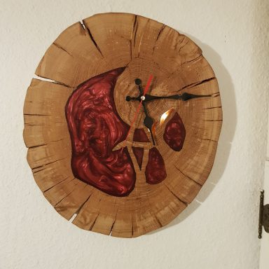 Wanduhr aus Holz mit rotem Epoxidharz und schwarzen Zeigern.